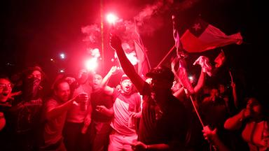Eine Gruppe von Demonstranten hält rot leuchtende und rauchende Lichter in die Höhe und schwenkt die chilenische Fahne.