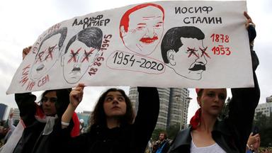 Drei Mädchen halten ein Plakat in die Höhe, auf dem vier Männerköpfe abgebildet sind