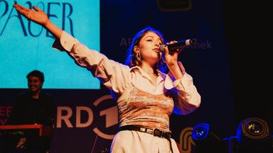 Eine junge Frau singt auf einer Bühne in ein Handmikrofon.