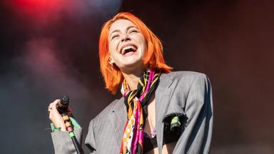 Eine junge Frau lacht auf einer Bühne, die Hand an einem Mikrofon.