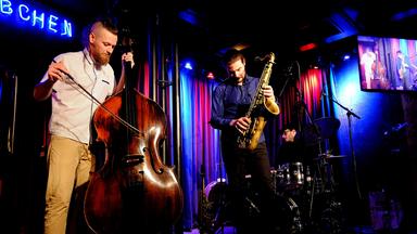 Zwei Musiker mit Kontrabass und Klarinette spielen auf einer blau und lila angeleuchteten Bühne.