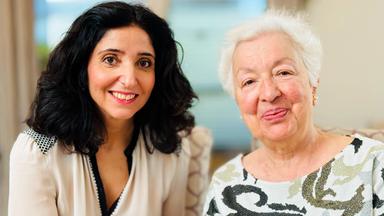 Eine ältere Dame mit weißem Haar sitzt neben der Moderatorin. Beide lächeln in die Kamera.