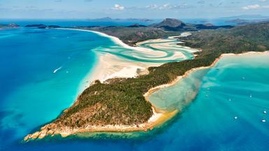 Luftaufnahme von Whitehaven Beach auf den Whitsunday Islands in Queensland. Weiße Sandbänke ziehen sich durch türkisblaues Wasser, umgeben von grünen Inseln.