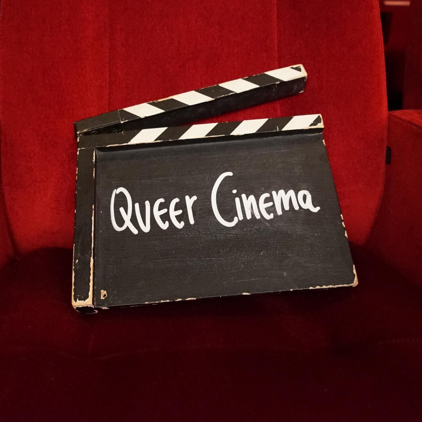 Eine Filmklappe mit der Aufschrift „Queer Cinema“ steht in einer Seitenische eines schmalen Ganges mit schwarzem Boden und roten Wänden.