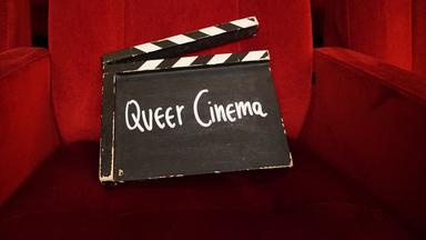 Eine Filmklappe mit der Aufschrift „Queer Cinema“ steht in einer Seitenische eines schmalen Ganges mit schwarzem Boden und roten Wänden.