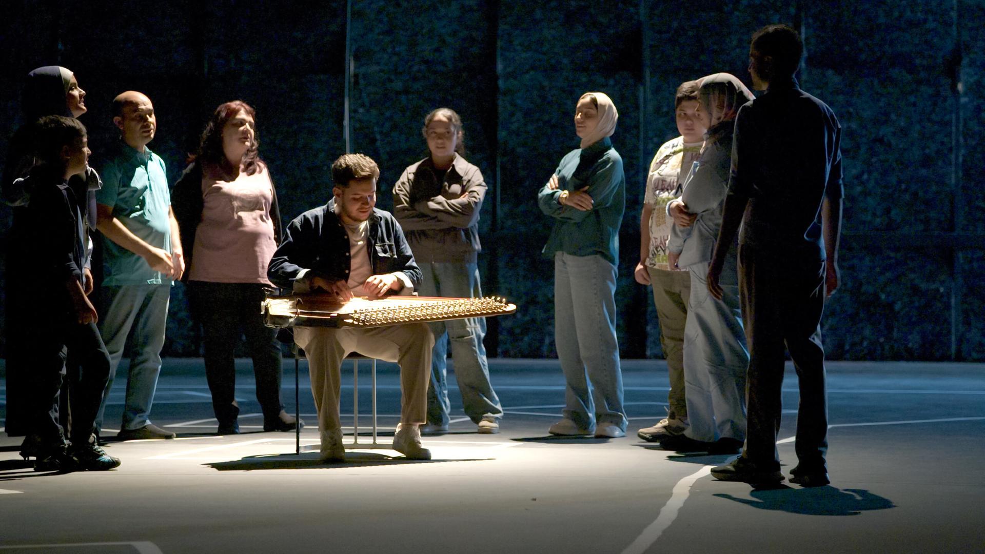 Auf einer Bühne steht eine Gruppe Menschen um einen Musiker, der ein orientalisches Zupfinstrument spielt.