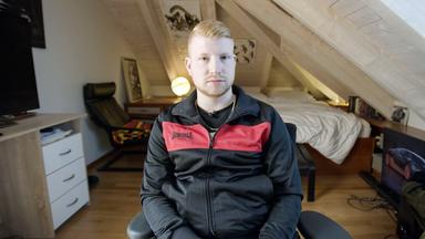 Ein junger Mann sitzt auf einem Stuhl in einem Schlafzimmer.