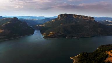 Eine dramatische Flusslandschaft in Bulgarien, umgeben von hohen Bergen unter einem bewölkten Himmel.
