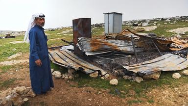 Ein Palästinenser im langen Kaftan mit traditionellem Tuch auf dem Kopf steht neben den Überresten eines zerstörten Hauses.