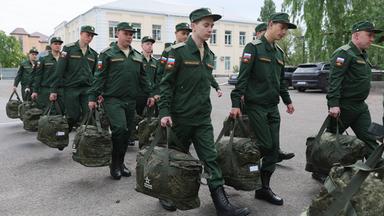 Eine Gruppe junger Männer in grüner Militäruniform trägt Camouflage-Taschen über einen Hof-