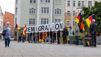 Frau mit Kopftuch geht an Demonstranten vorbei, die Buchstaben des Schriftzugs "Remigration" hochhalten.