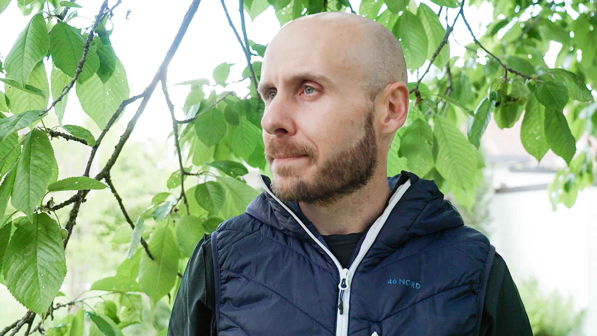 Lukas Bissegger vor Zweigen mit grünen Blättern.