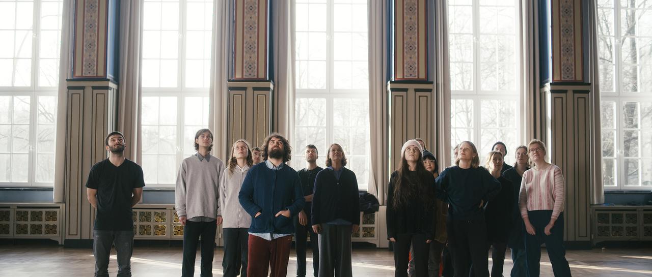Eine Gruppe junger Menschen blickt nach oben, im Hintergrund große Fenster.