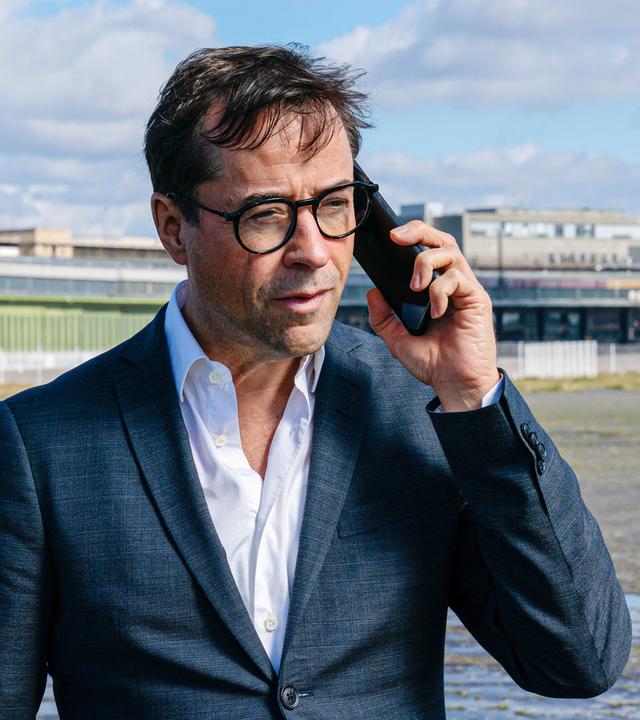 Mann hält auf einem zugigen Gelände eine Smartphone ans Ohr.