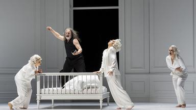 Drei weiss gekleidete Frauen bewegen sich mit einem schwarz gekleideten Mann um eine weisse Bank