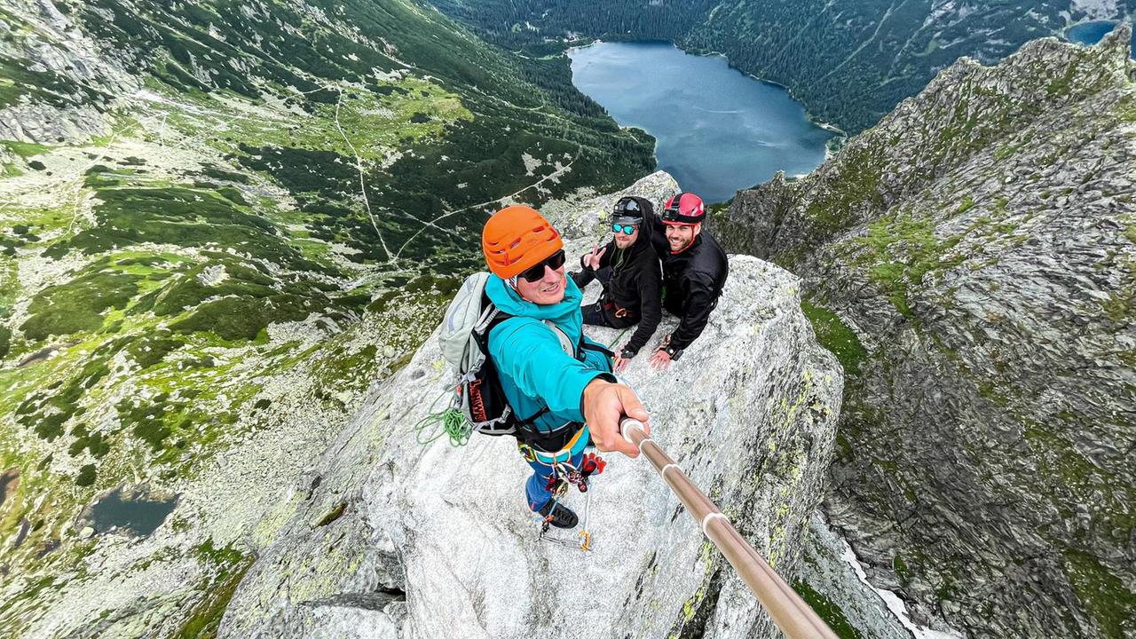 Blick von oben auf drei Menschen in Kletter-Ausrüstung, die auf einem Berg stehen