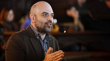 Ein Mann mit Glatze und Bart spricht in ein Mikrofon.