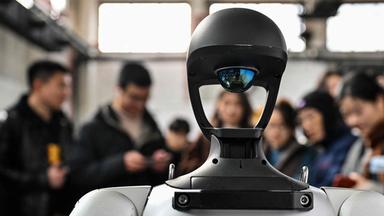 Ein humanoider Roboter wird bei einer Messe von Menschen umringt, die ihn betrachten.