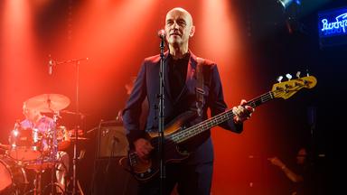 Ein Mann spielt Gitarre an einem Standmikrofon.