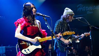 Eine Frau und ein Mann am Mikro mit E-Gitarre auf einer Bühne