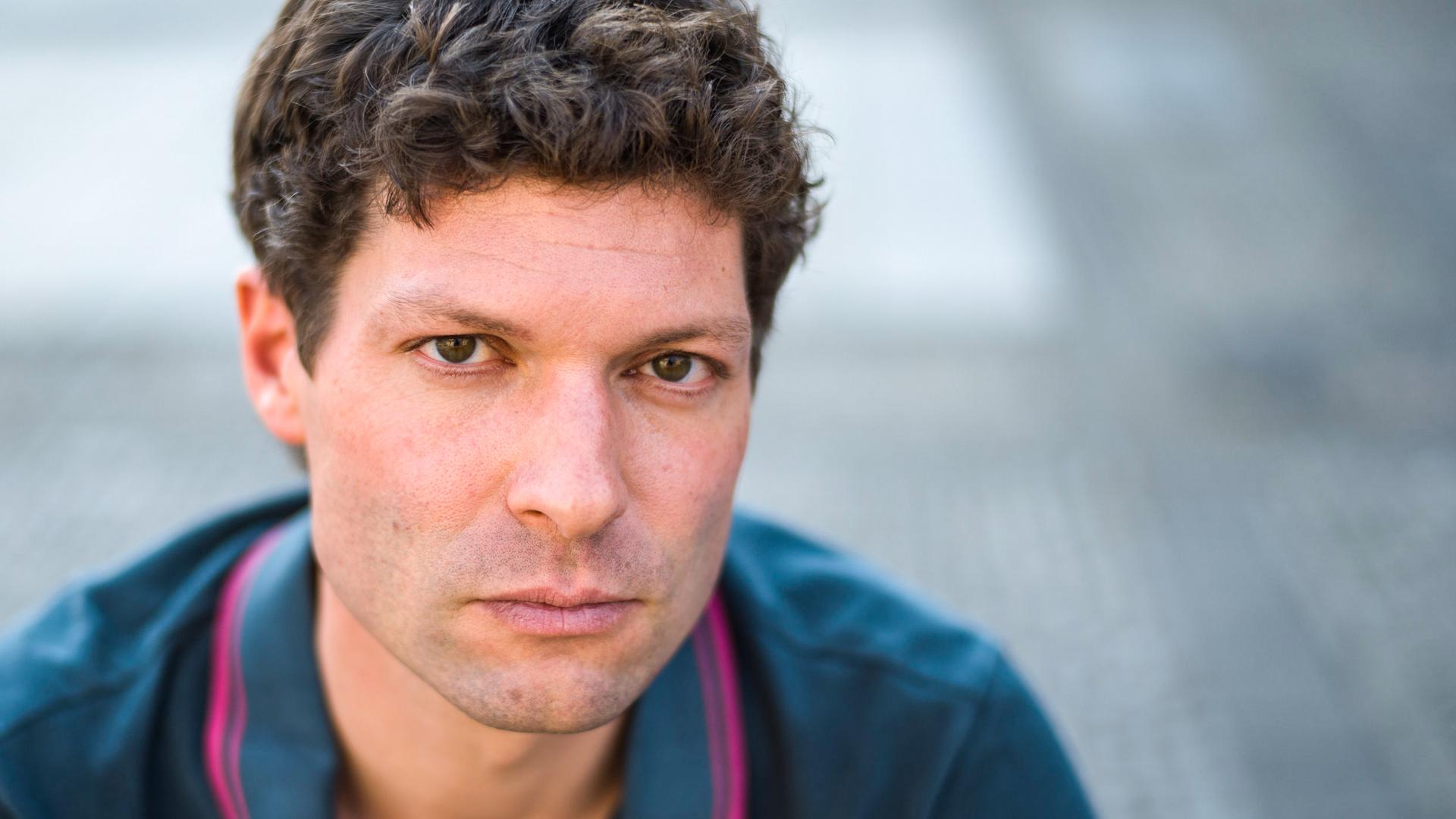 Ein Mann mit braunem Haar schaut in die Kamera.