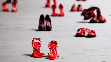 Auf einem Platz stehen in unregelmäßigen Abständen unterschiedliche rote Frauenschuhe.