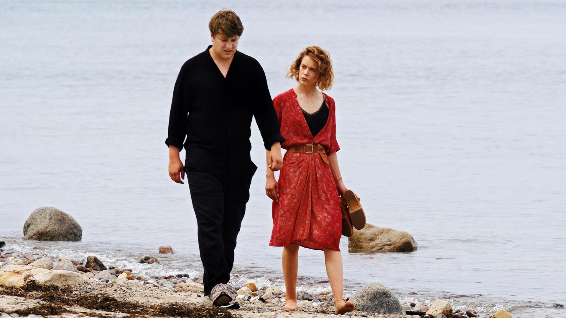 Leon (Thomas Schubert) und Nadja (Paula Beer) laufen nebeneinander am Strand entlang.