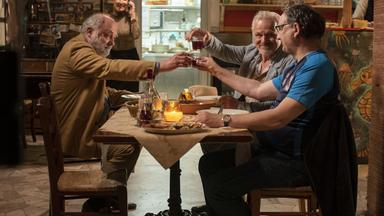 Drei Männer prosten sich an einem Tisch zu.