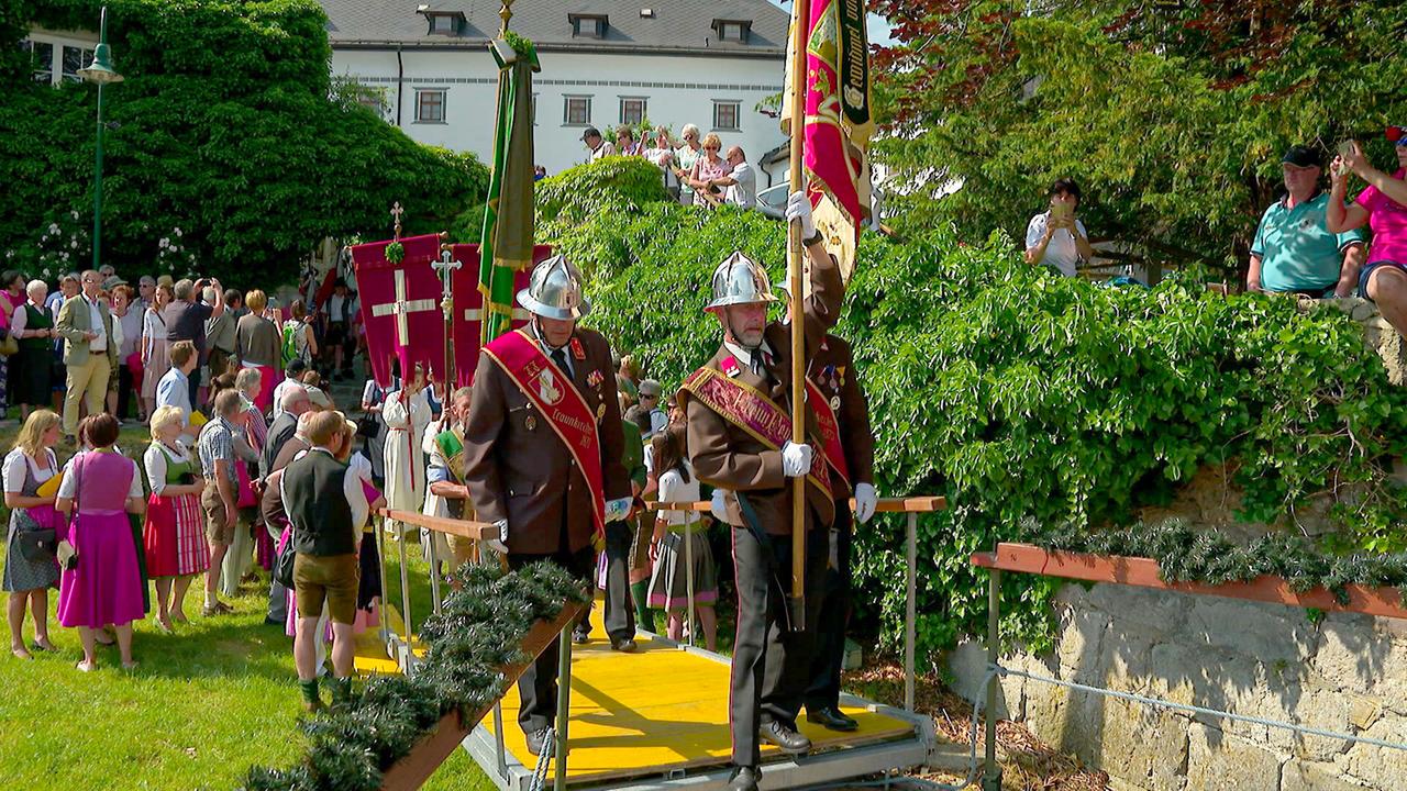 Menschen mit Fahnen in Uniformen und Trachten versammeln sich in einr Parkanlage