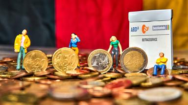 Modellbau-Menschen auf Geldstücken mit deutscher Fahne im Hintergrund 