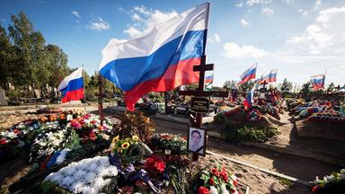 Über frischen Gräbern mit vielen Blumenkränzen und Fotos der verstorbenen wehen weiß-blau-rote Flaggen