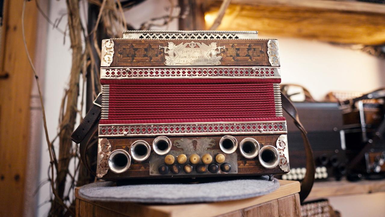 Eine historische Harmonika mit rotem Balg und kunstvollen Verzierungen steht auf einem Holztisch in einer traditionellen Werkstatt.
