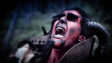 Ein als Teufel verkleideter Darsteller mit roten Gesichtszügen, schwarzen Hörnern und aufgerissenem Mund in einer dramatischen Szene.