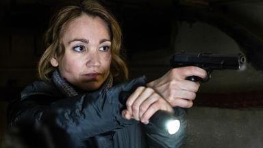 Eine Frau hält in der rechten Hand eine Pistole, in der linken eine Taschenlampe. 