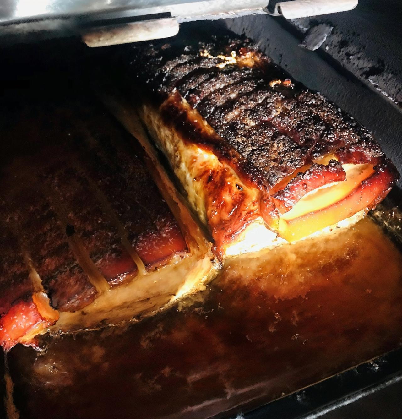 Auf dem Bild ist ein Braten, vermutlich ein Schweinsbraten, der im Ofen zubereitet wird. Der Braten ist von einer knusprigen, dunkelbraunen Kruste umgeben, die Stellen von gebräuntem Fett aufweist. Die Oberfläche ist wellig und hat einige Einschnitte, die wahrscheinlich die Kruste verbessern.   Im Hintergrund ist der Ofen sichtbar, dessen Innenraum dunkel ist. Der Braten liegt in einer metallischen Form, die mit einer bräunlichen Sosse oder Fett gefüllt ist. Die Beleuchtung im Bild ist diffus, was eine angenehme, warme Atmosphäre schafft.   Dieser Schweinsbraten ist ein bekanntes Gericht aus Oberösterreich und wird oft mit Beilagen wie Sauerkraut oder Knödeln serviert.