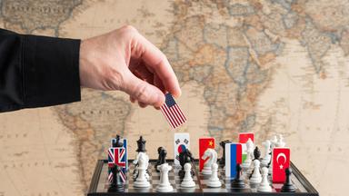 Eine Hand nimmt eine Spielfigur mit US-amerikanischer Flagge von einem Schachspiel, auf dem Länderflaggen verteilt sind.