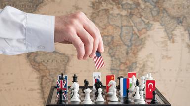 Eine Hand nimmt eine Spielfigur mit US-amerikanischer Flagge von einem Schachspiel, auf dem Länderflaggen verteilt sind.