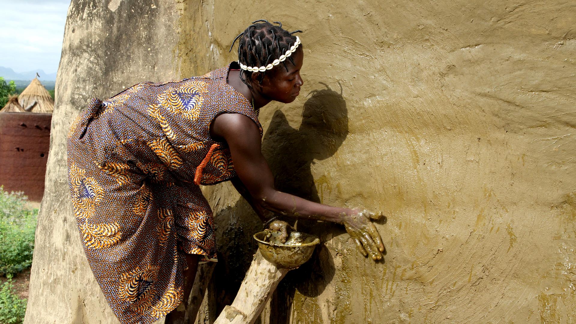 Eine Frau beim Präparieren der Lehmwand mit Kuhdung. 