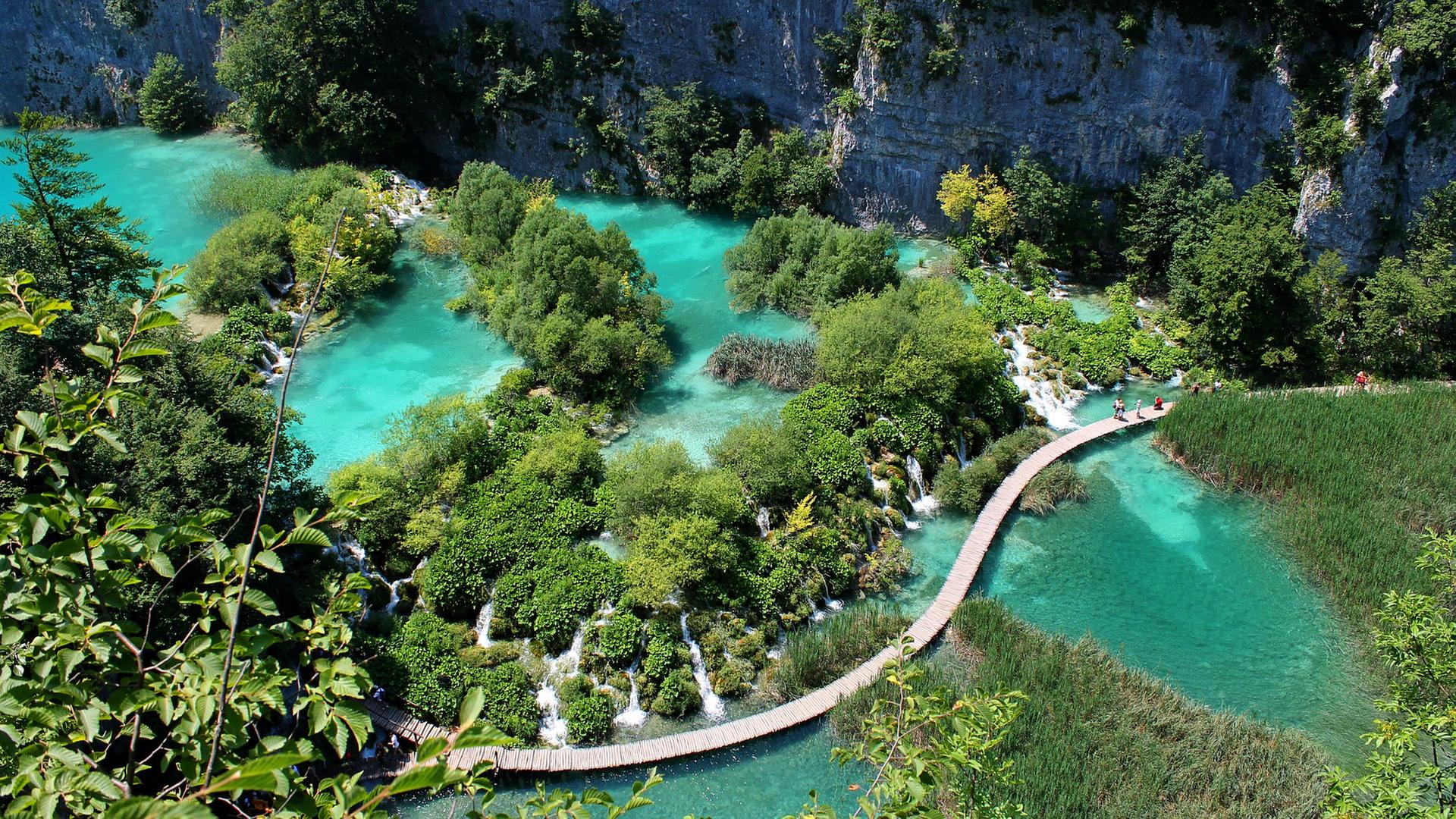 Ein langer Holzsteg führt durch den Nationalpark vorbei an Wasserfällen und türkisfarbenen Seen.
