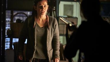 "Schattengrund": Nicola Wagner (Josefine Preuß) steht im Keller und sieht verängstigt zu der Frau, die vor ihr steht. Diese ist nur unscharf von hinten zu sehen, wie sie eine Waffe auf Nicola richtet.