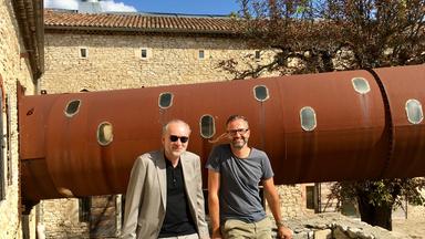 Der Schriftsteller Ferdinand von Schirach und Filmautor Claudio Armbruster lehnen an einer Steinmauer vor dem Haus des Künstlers Anselm Kiefer in Barjac, Südfrankreich.