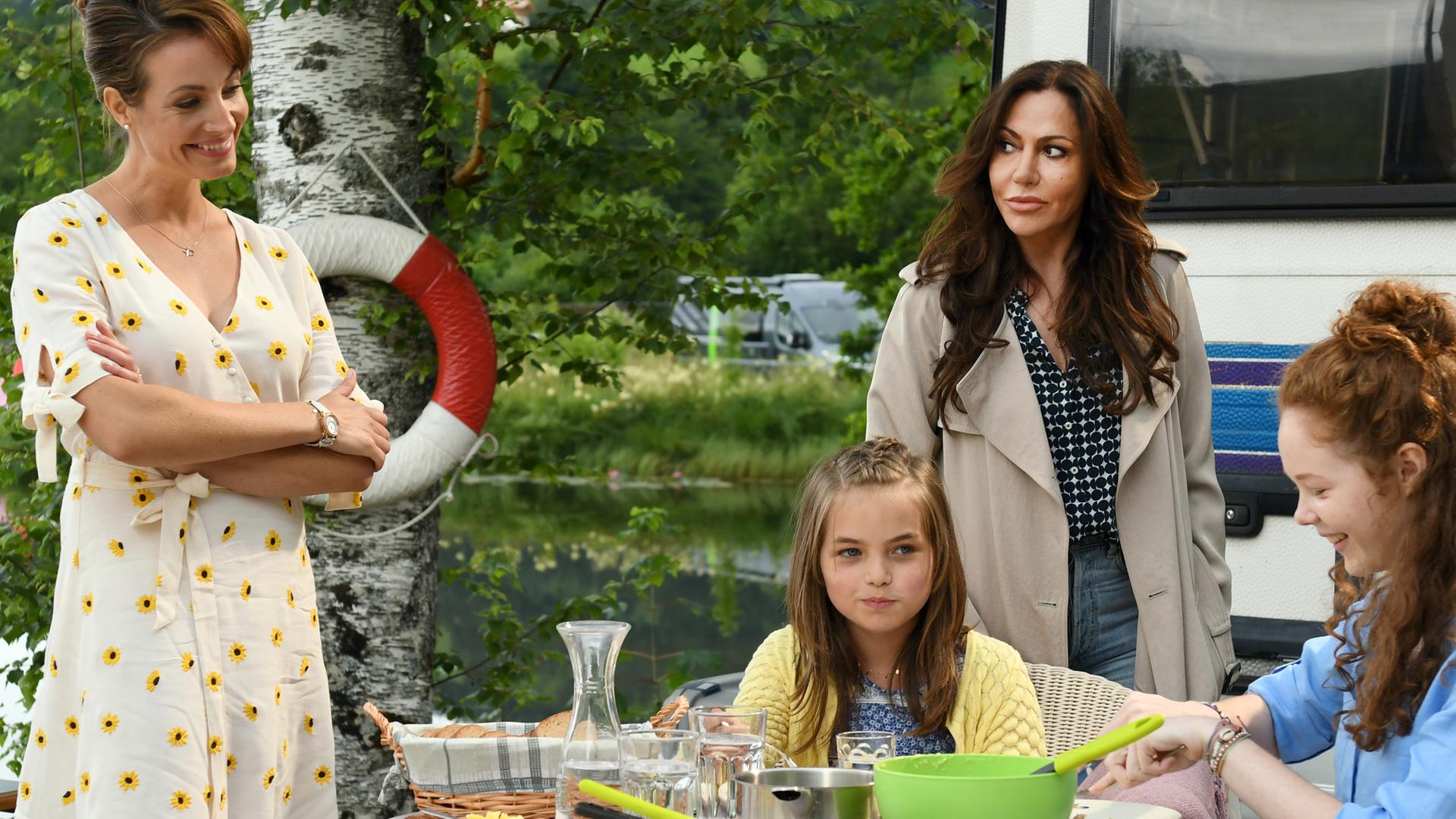 Katja Baumann (Simone Thomalla) und Frau Zerbe (Dagny Dewath) stehen neben dem Frühstückstisch, an dem Charlotte (Lilli Schweiger) und Greta (Theresia Vajkoczy) sitzen.