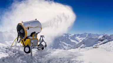Eine Schnee aussprühende Schneekanone vor strahlend blauem Himmel im Einsatz