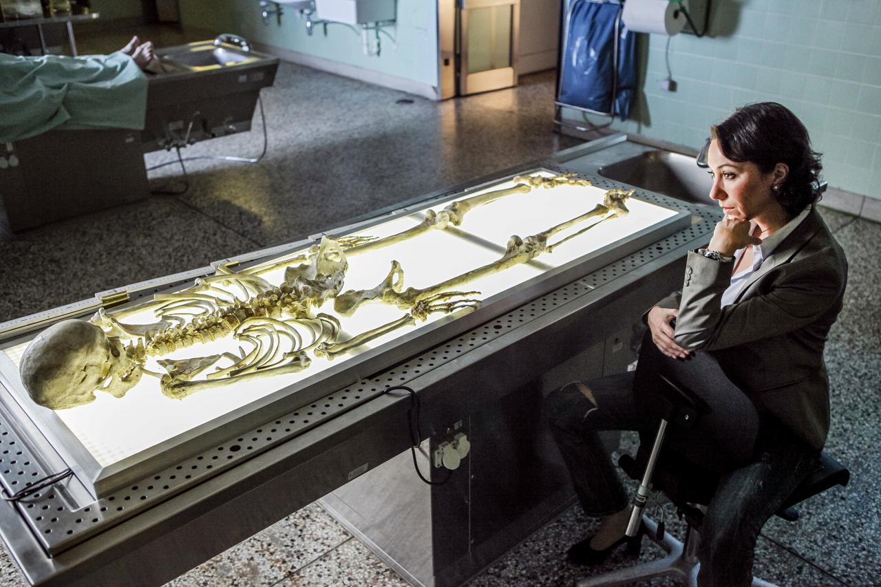 eine frau sitzt vor einem labortisch mit einem darauf liegenden skelett