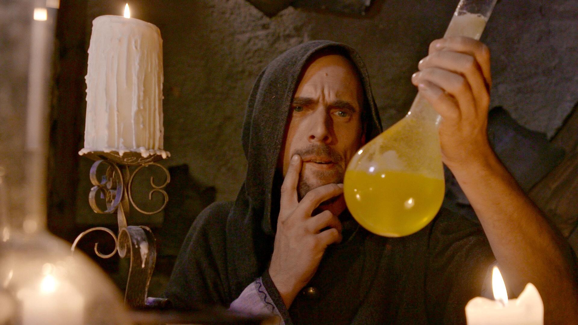 Ein Alchemist in dunkler Kutte betrachtet nachdenklich eine mit gelber Flüssigkeit gefüllte Glasflasche in einem schummrig beleuchteten Labor mit Kerzenlicht.