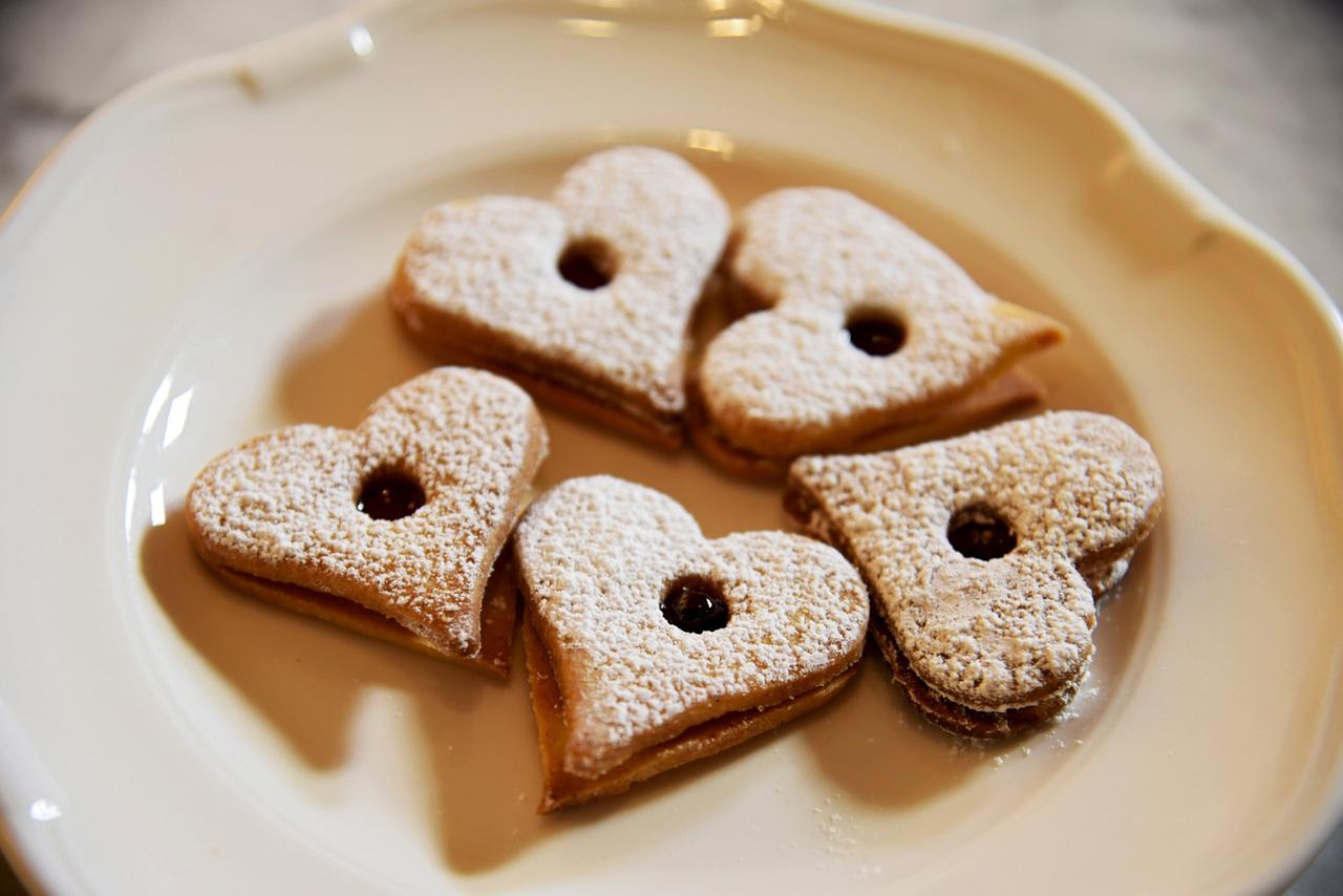 Fünf herzförmige Kekse mit Puderzucker bestreut, liegen auf einem Teller.