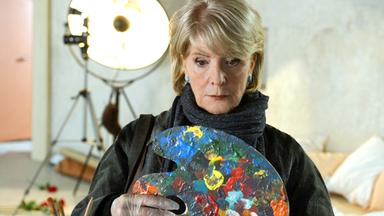 Die Darstellerin schaut bestürzt auf eine Malerpalette