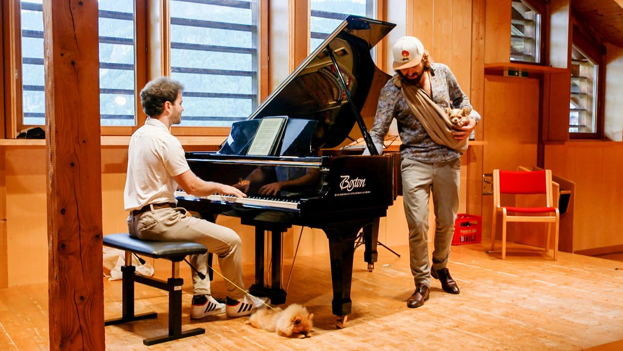 Ein Mann sitzt am Flügel und ein anderer Mann steht daneben.