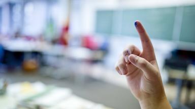 Schüler meldet sich mit hoch gestrecktem Finger im Klassenzimmer.