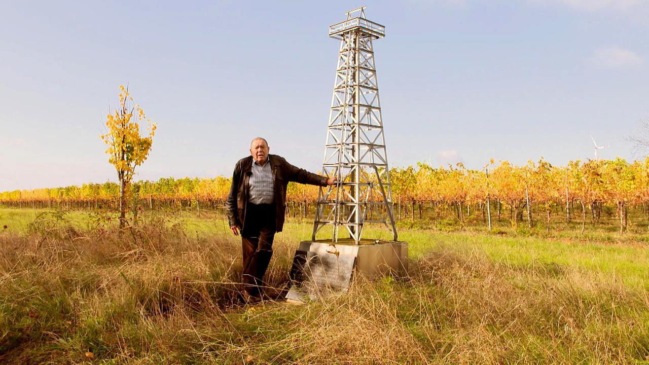 Mann lehnt sich an einen Metallturm auf einem Feld